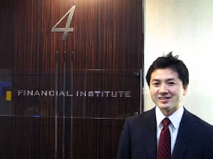 株式会社フィナンシャル・インスティチュートの社名ロゴを背景に立つ川北氏の写真