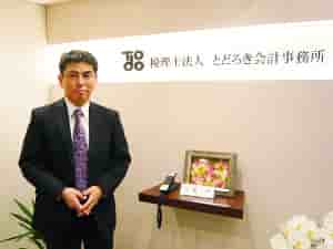 税理士法人とどろき会計事務所のロゴを背景に立つ轟勝之氏の写真